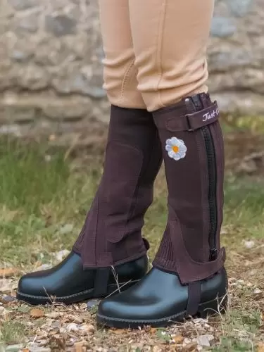 A side view of a young child wearing a wearing a pair of brown half chaps with daisy motif by Just Chaps