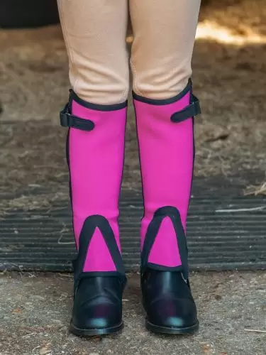 A young child wearing a pair of bright pink half chaps in neoprene by Just Chaps