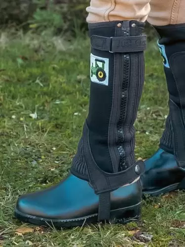 A side view of a child wearing a pair of Dinky half chaps for toddlers in black with a tractor motif by Just Chaps