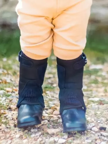 A front view of a toddler wearing a pair of dinky half chaps in black neoprene by Just Chaps