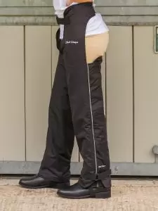 Young horse rider standing by stable door wearing at pair of Dri-Rider fleece lined full chaps in black by Just Chaps