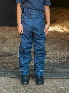 A close up image of a child standing in stable door wearing a pair of kids Dri-Rider waterproof riding trousers in navy by Just Chaps