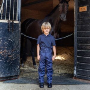 young rider wearing waterproof trousers and standing at the entrance to the stable